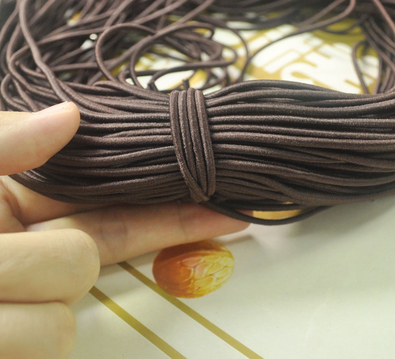 May include: A close-up of a large spool of brown elastic cord. The cord is tightly wound and appears to be made of a soft, stretchy material.
