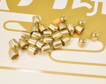 Puede incluir: Un montón de tapones de metal dorado para cordones o joyas. Los tapones son redondos y tienen un pequeño agujero en la parte superior.