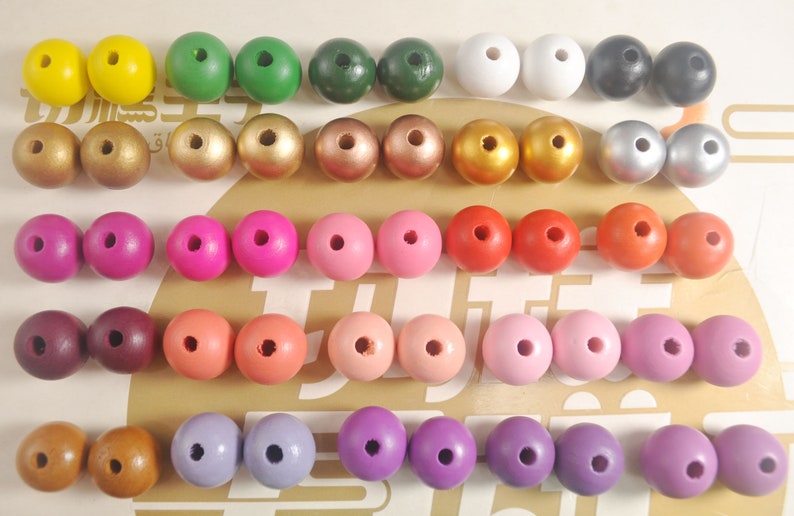 May include: A collection of 40 wooden beads in various colors, including yellow, green, white, black, gold, silver, pink, red, brown, and purple. The beads are arranged in rows on a light brown surface.
