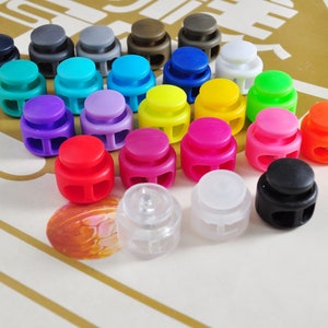 May include: Assortment of colorful plastic toggle clasps with two holes. The clasps come in a variety of colors, including red, orange, yellow, green, blue, purple, pink, black, and white.