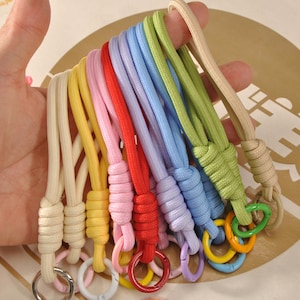 Può includere: Una collezione di cordini colorati in varie tonalità, tra cui crema, giallo, rosa, rosso, lavanda, blu, verde e beige. Ogni cordino presenta un cordoncino abbinato e un anello metallico.