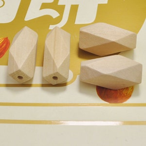 Może przedstawiać: Cztery nieoszlifowane drewniane koraliki o fasetowanym, geometrycznym kształcie. Każdy koralik ma otwór przewiercony przez środek.