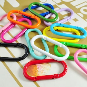 May include: Assortment of colorful metal oval-shaped keychains. The keychains are in various colors, including black, pink, green, blue, yellow, and red.