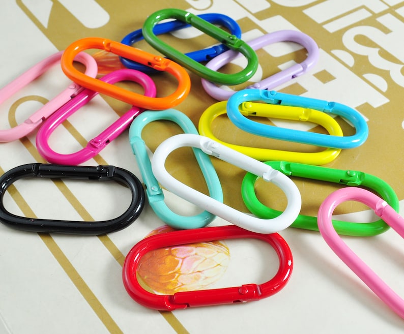 May include: Assortment of colorful metal oval-shaped keychains. The keychains are in various colors, including black, pink, green, blue, yellow, and red.