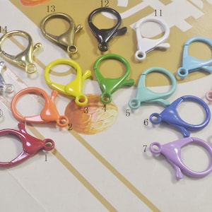 May include: Assortment of 16 colourful metal keyrings with spring-loaded clasps. The keyrings are in various colours, including red, orange, yellow, green, blue, purple, pink, and silver.