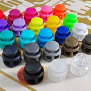 May include: Assortment of colorful plastic toggle clasps, also known as cord locks, in various colors including red, blue, green, yellow, purple, gray, and white.
