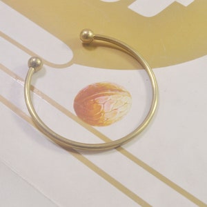 May include: A simple gold bangle bracelet with rounded ends. The bracelet is made of a smooth, shiny metal.