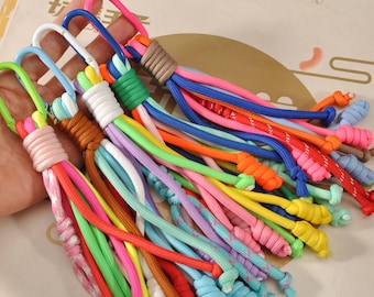 May include: A collection of colorful keychains with various colored cords and metal carabiner clips. The keychains feature a variety of bright colors, including pink, blue, green, yellow, and orange. Each keychain has a unique design and color combination.