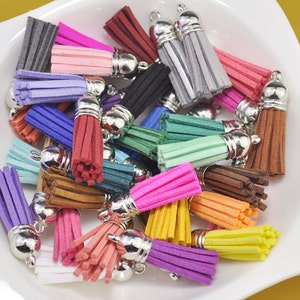 Puede incluir: Surtido de borlas de gamuza de colores vivos con tapas de metal plateado. Las borlas están dispuestas en un cuenco y son de varios tonos de azul, verde, rosa, rojo, naranja, amarillo, marrón y morado.