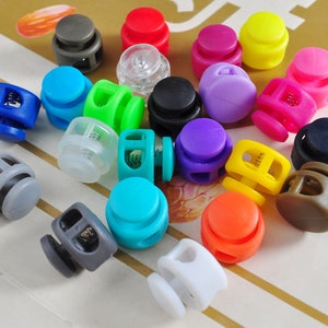 May include: Assortment of colorful plastic toggle clasps, including blue, green, yellow, red, purple, orange, white, gray, black, and brown. The clasps are used for securing cords, straps, or other items.