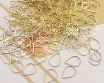 May include: A large pile of gold-colored metal teardrop-shaped earring blanks. There are several individual teardrop blanks scattered around the pile.