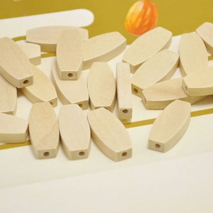 May include: A pile of 20 natural wood oval beads with a hole through the centre. The beads are light brown and have a smooth finish.