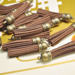 May include: A group of brown suede tassels with antique gold metal caps. The tassels are approximately 2 inches long.