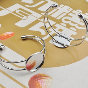 May include: Two silver metal bangle bracelets with a round, clear glass cabochon in the center of each. The bracelets are open and ready to be worn.