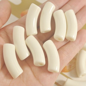 Puede incluir: Una colección de cuentas de plástico curvadas de color blanco roto. Las cuentas son lisas y brillantes.