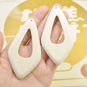 May include: Two unfinished, white wood, teardrop-shaped earrings with a hole at the top for hanging.