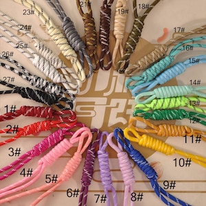Puede incluir: Una colección de cordones coloridos en varios tonos, incluyendo rojo, rosa, morado, azul, verde, amarillo, marrón y gris. Cada cordón está numerado y presenta un diseño trenzado. Los cordones son probablemente para sujetar llaves, identificaciones u otros objetos pequeños.