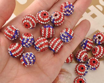 May include: A selection of red, white, and blue rhinestone beads. The beads are spherical with a hole through the middle. The beads are a mix of red, white, and blue rhinestones, with some beads having stripes and others having solid colours.