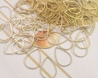 May include: A large pile of gold-colored metal teardrop-shaped earring blanks. The blanks are arranged in a random pattern and are all the same size.