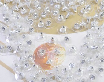 May include: A large quantity of clear plastic earring backs with silver metal posts. The backs are round and have a slight dome shape.
