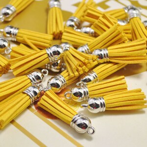 Peut inclure: Un groupe de glands en daim jaune avec des embouts en métal argenté. Les glands sont disposés en pile sur une surface rayée.