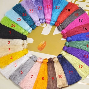May include: A collection of 26 colorful tassel trims, arranged in a circle. The tassels are made of various materials, including silk, cotton, and wool. The colors include black, white, yellow, orange, red, pink, purple, blue, green, and brown.