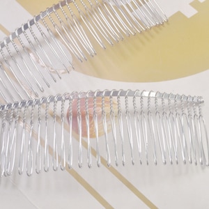 Pode incluir: Dois pentes de cabelo prateados com forma curva e design de fio trançado. Os pentes têm muitos dentes finos.