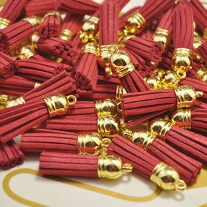 Könnte beinhalten: Ein Haufen roter Samtquasten mit goldenen Metallkappen. Die Quasten sind etwa 5 cm lang und haben eine Franse am unteren Ende.