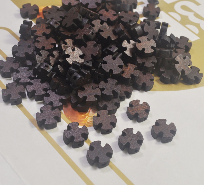 Puede incluir: Un mont&oacute;n de cuentas de madera marr&oacute;n oscuro con forma de estrella de cuatro puntas. Las cuentas est&aacute;n esparcidas sobre una superficie blanca con rayas doradas.