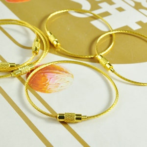 May include: Four gold-colored cable keychains with a metal clasp. The keychains are arranged in a circle on a white surface.