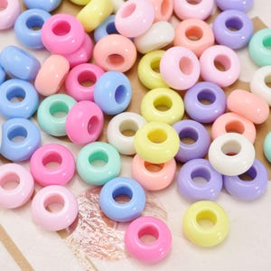 May include: A collection of colorful, round beads in various pastel shades, including pink, blue, yellow, green, and purple. The beads have a donut shape with a hole in the center, perfect for jewelry making or crafting projects.