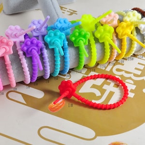 Könnte beinhalten: Sortiment an bunten Silikon-Kabelbindern mit Pfotenabdrücken. Die Bänder sind von 1 bis 17 nummeriert.