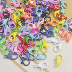 Op de afbeelding: Een grote verzameling kleurrijke metalen lobster-sluitingen. De sluitingen zijn in verschillende kleuren, waaronder rood, blauw, groen, geel, paars en wit.