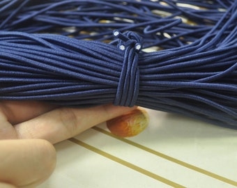 May include: A close-up of a large spool of navy blue elastic cord. The cord is tightly wound and has a white knot at the end.