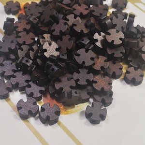 Puede incluir: Un mont&oacute;n de botones de madera marr&oacute;n oscuro con forma de estrella de cuatro puntas. Los botones tienen una superficie rugosa y texturizada.