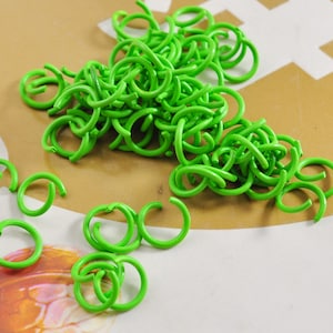 Puede incluir: Un montón grande de anillos de salto de metal verde brillante. Los anillos son todos del mismo tamaño y están dispuestos en un patrón aleatorio.