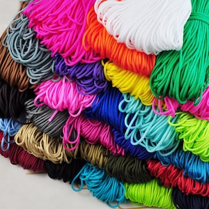 May include: A collection of brightly coloured nylon cords in a variety of shades, including pink, green, orange, and blue. The cords are bundled and neatly arranged, showcasing a range of hues suitable for crafting and DIY projects.