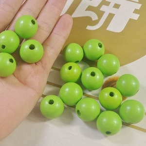 May include: A collection of 15 bright green wooden beads with a hole in the center. The beads are arranged in a pile on a white surface.