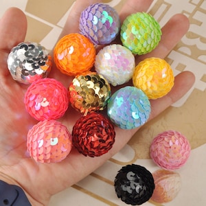 Op de afbeelding: Een verzameling kleurrijke, met pailletten versierde balornamenten in verschillende kleuren, waaronder zilver, oranje, paars, groen, wit, geel, roze, goud, rood, blauw en zwart. Deze decoratieve bollen zijn ideaal voor knutselprojecten of feestversieringen.