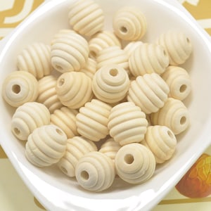 以下が含まれることがあります： ハニカム模様のナチュラルウッドビーズのボウル。ビーズは薄いクリーム色で、滑らかで磨かれた仕上げになっています。