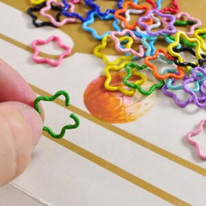 K&ouml;nnte beinhalten: Eine Sammlung von bunten sternf&ouml;rmigen Metallringen. Die Ringe sind aus Draht gefertigt und in verschiedenen Farben erh&auml;ltlich, darunter Rot, Orange, Gelb, Gr&uuml;n, Blau, Lila und Pink.
