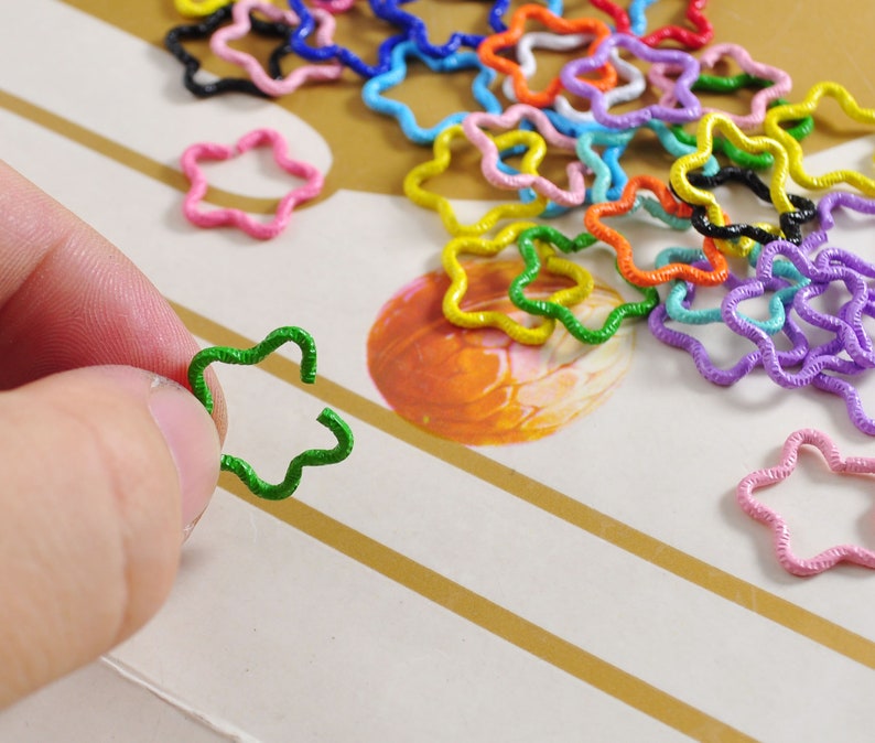 K&ouml;nnte beinhalten: Eine Sammlung von bunten sternf&ouml;rmigen Metallringen. Die Ringe sind aus Draht gefertigt und in verschiedenen Farben erh&auml;ltlich, darunter Rot, Orange, Gelb, Gr&uuml;n, Blau, Lila und Pink.
