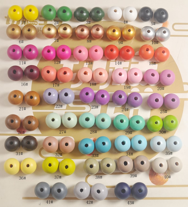 May include: A collection of 43 wooden beads in various colors, arranged in rows on a white surface. Each bead is numbered with a black marker.