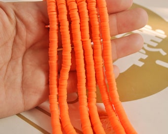 May include: A close-up of a strand of orange polymer clay beads. The beads are flat and round, and they are stacked on top of each other. The beads are strung on a clear elastic cord.