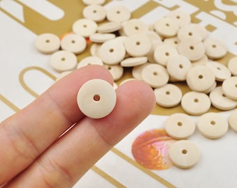 May include: A close-up of a wooden bead with a hole in the center. The bead is light brown and has a smooth surface. The bead is being held by a finger.