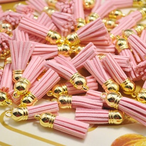 Könnte beinhalten: Ein Haufen rosa Samtquasten mit goldenen Metallkappen. Die Quasten sind etwa 5 cm lang.