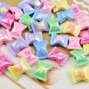 May include: Assortment of colorful candy-shaped plastic beads with a sweet design and a bunny rabbit image. The beads are iridescent and have a glossy finish.