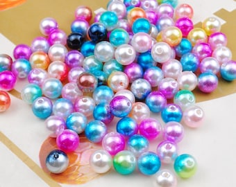 May include: A large assortment of iridescent pearl beads in various colors, including pink, blue, green, and purple. The beads are scattered on a light brown surface.