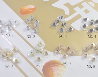 May include: Eight different styles of clear plastic earring backs with metal posts. The backs are arranged in rows of two, with each row labeled with a number from 1 to 8.