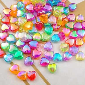 Può includere: Un vasto assortimento di perline a forma di cuore iridescenti in vari colori, tra cui rosa, verde, blu, giallo e arancione. Le perline sono in plastica e hanno una finitura liscia e lucida.